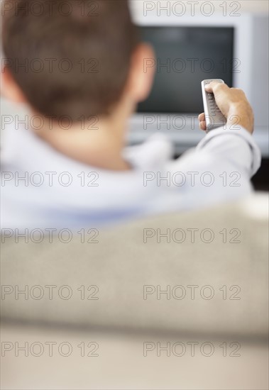 Mid adult man in front of televisionchanging channels. Photo : Momentimages