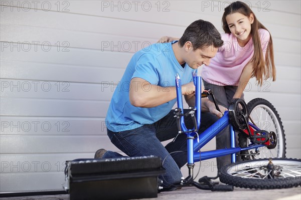 Father with daughter (10-11) fixing bike. Photo : Momentimages