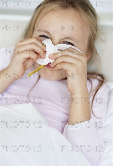 Girl (10-11) blowing nose with thermometer in mouth. Photo : Momentimages
