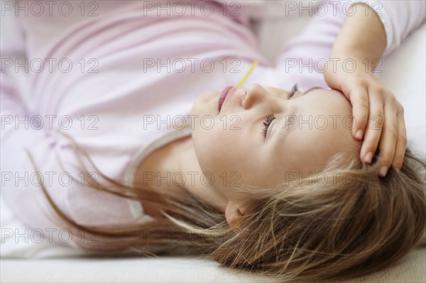 Sad girl (10-11) lying in bed with thermometer in mouth. Photo : Momentimages