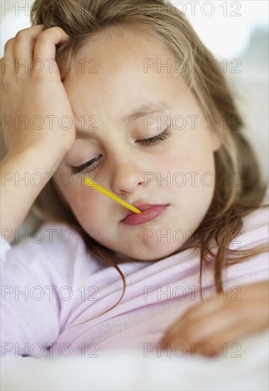 Sad girl (10-11) lying in bed with thermometer in mouth. Photo : Momentimages