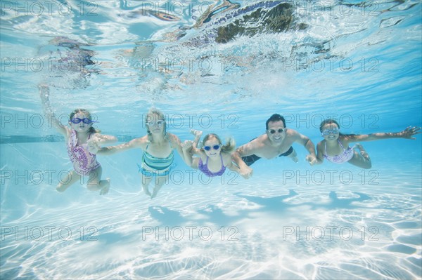 Family with three daughters (4-5,6-7,8-9) swimming underwater.