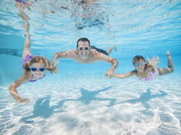 Father with two daughters (6-7,8-9) swimming underwater.