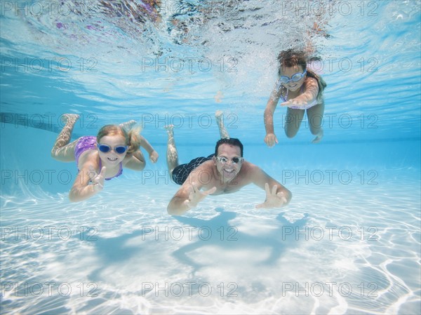 Father with two daughters (6-7,8-9) swimming underwater.