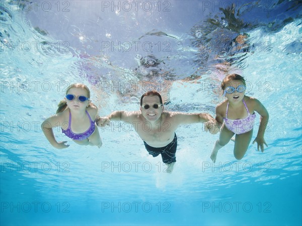 Father with two daughters (6-7,8-9) swimming underwater.