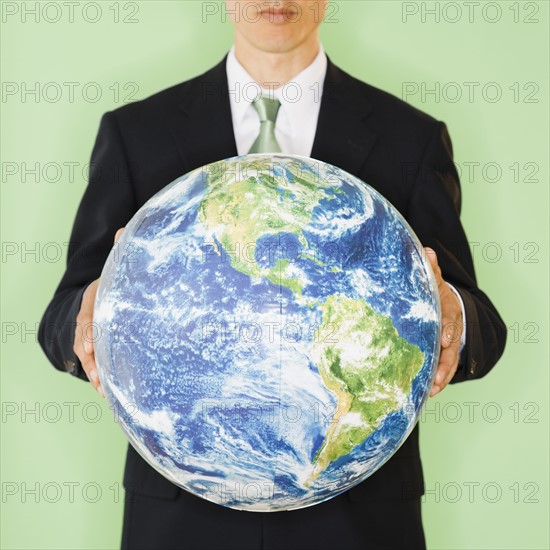 Businessman holding globe, studio shot. Photo : Jamie Grill