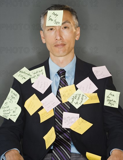 Businessman with post-it sticking on him, studio shot. Photo : Jamie Grill