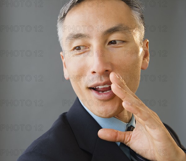 Businessman covering face and whispering, studio shot. Photo : Jamie Grill