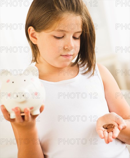 Girl (8-9) holding piggybank and coins. Photo : Daniel Grill