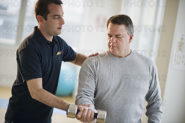 USA, New Jersey, Jersey City, Fitness instructor assisting man using hand weight in gym.