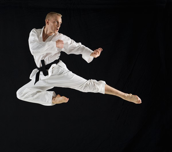 Young man performing karate kick on black background.