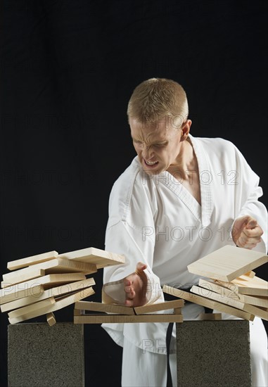 Young man breaking boards with karate chop on black background.