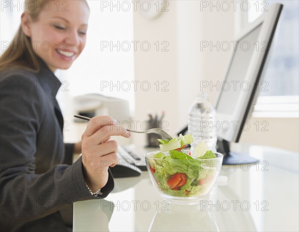 USA, New Jersey, Jersey City, young businesswoman eating salad in office. Photo : Jamie Grill Photography