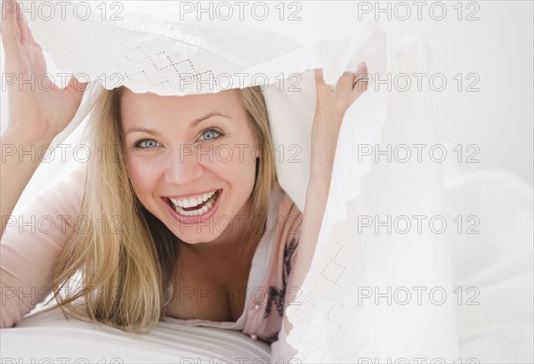 USA, New Jersey, Jersey City, Laughing attractive young woman emerging from under quilt. Photo : Jamie Grill Photography