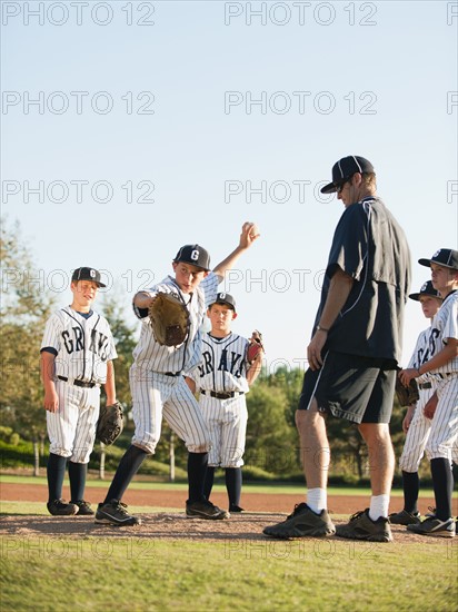 Baseball coach and boys (10-11) standing on baseball diamond.