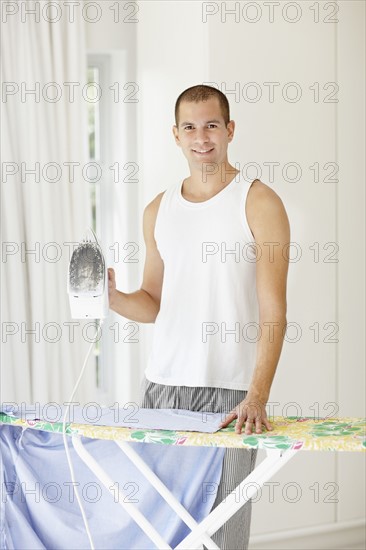 South Africa, Portrait of young man ironing shirt. Photo : momentimages