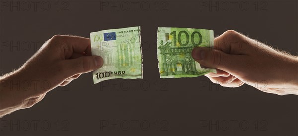 Hands holding torn one hundred euro note. Photo : Mike Kemp