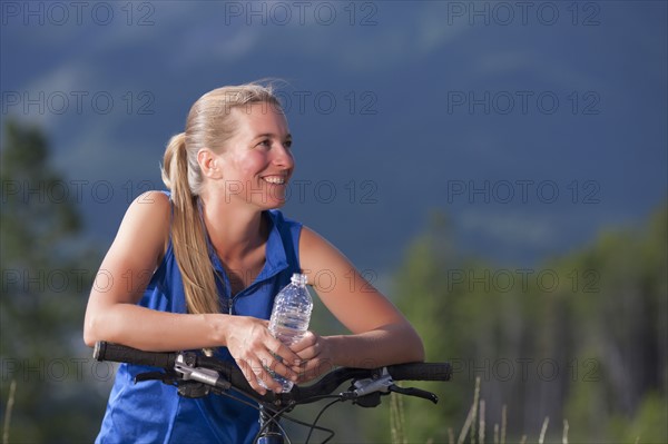 Canada, British Columbia, Fernie, Mid adult woman leaning against bike handlebar and drinking water. Photo : Dan Bannister