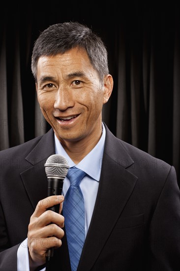 USA, Utah, Provo, Portrait of businessman with microphone standing in front of black curtain. Photo : FBP