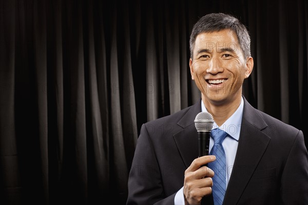 USA, Utah, Provo, Portrait of businessman with microphone standing in front of black curtain. Photo : FBP