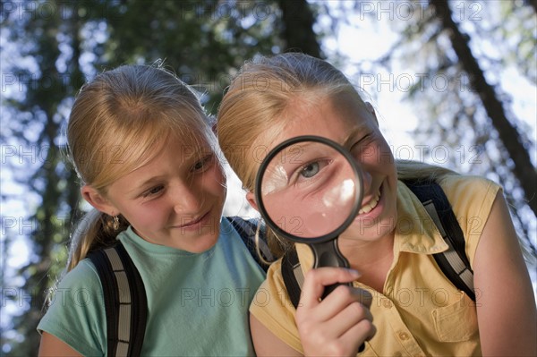 Canada, British Columbia, Fernie, sisters looking through magnifying glass. Photo : Dan Bannister