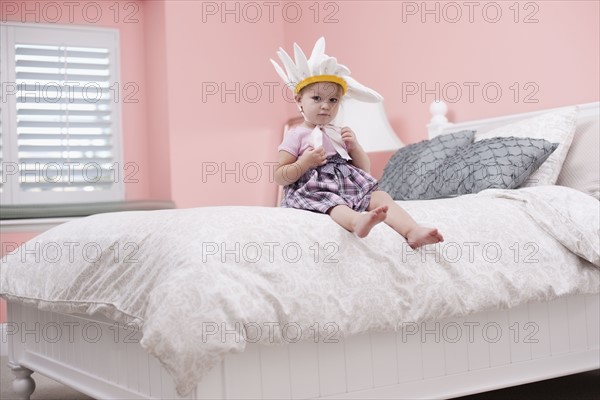 USA, Utah, small girl (2-3) with plume sitting on bed. Photo : Tim Pannell