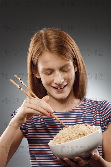 Portrait of redhead girl (10-11) holding chopsticks and bowl of rice, studio shot. Photo : FBP