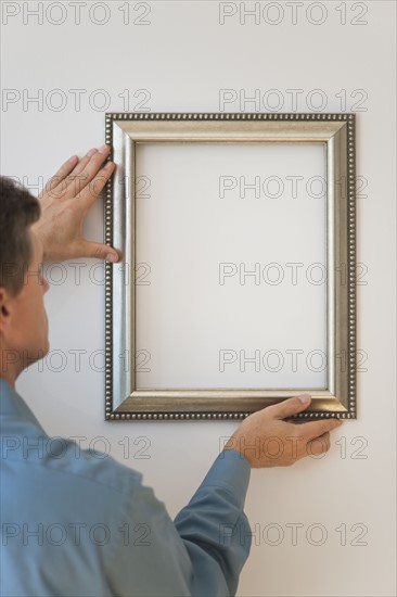 Man hanging silver frame on wall.