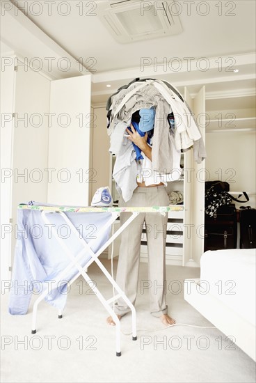 South Africa, Man standing with pile of laundry in front of ironing board. Photo : momentimages