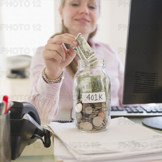 USA, New Jersey, Jersey City, Businesswoman putting money into piggybank. Photo : Jamie Grill Photography