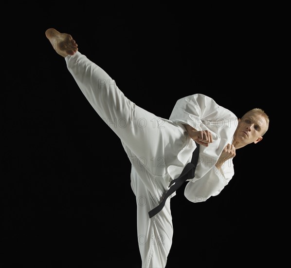 Young man performing karate kick on black background.