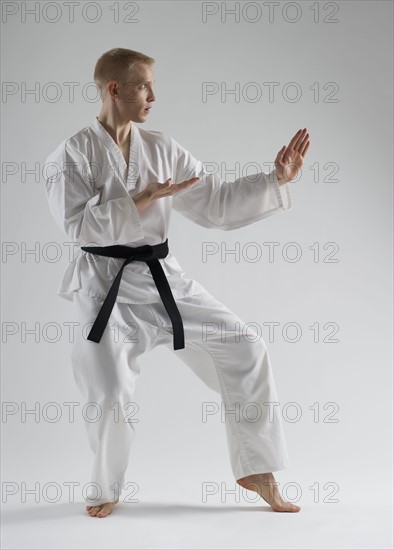 Young man performing karate stance on white background.