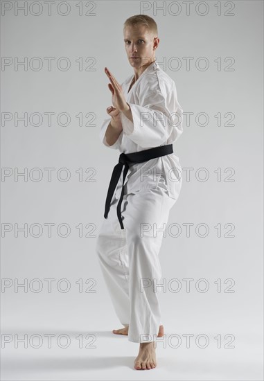 Young man performing karate stance on white background.