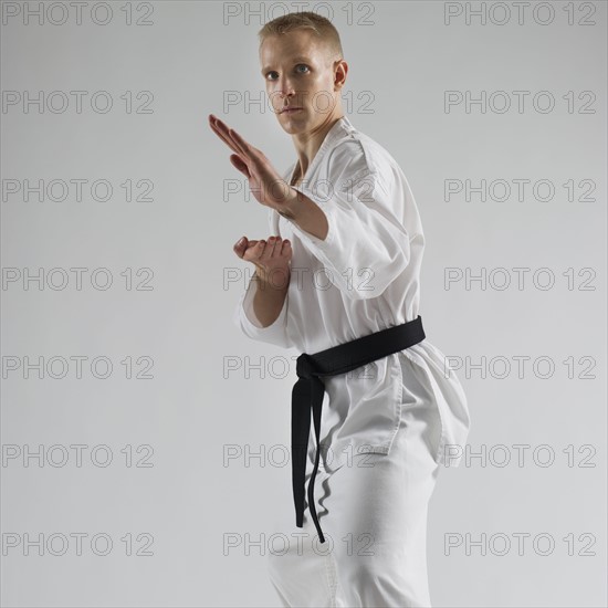 Young man performing karate stance on white background.