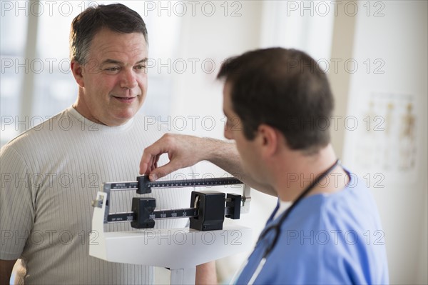 USA, New Jersey, Jersey City, Doctor assisting male patient on weighing scales in hospital.