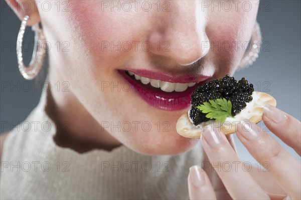 Young woman eating caviar on biscuit.