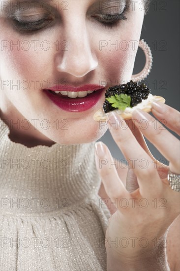 Young woman eating caviar on biscuit.