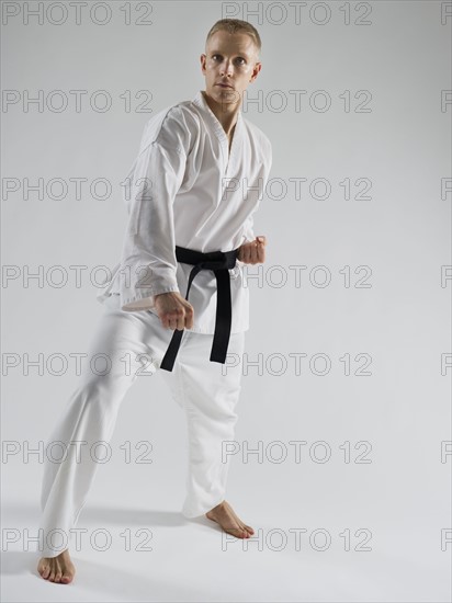 Young man performing karate stance on white background.