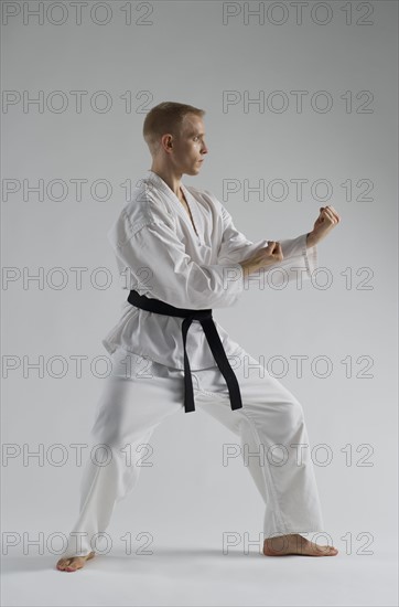 Young man performing karate stance on white background.