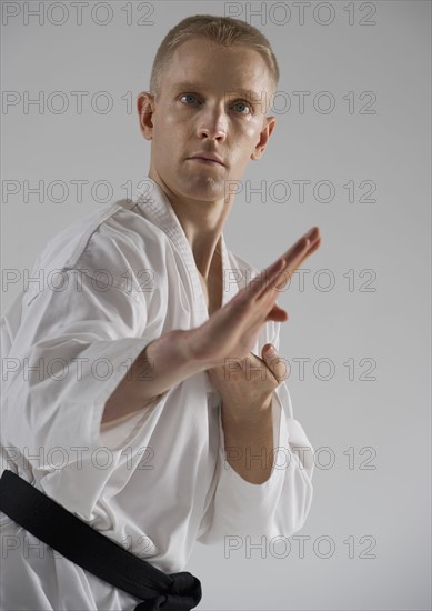 Young man performing karate stance on white background.