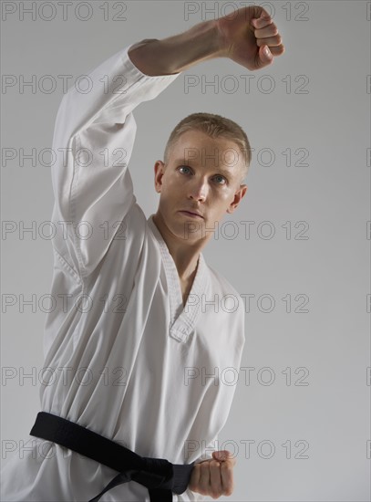 Young man performing karate stance on white background.