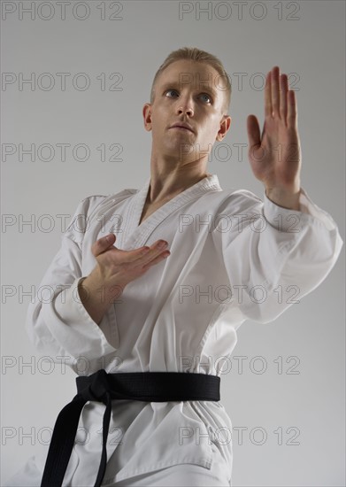 Young man performing karate stance on white background.