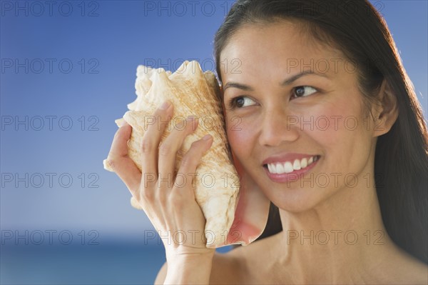 USA, New Jersey, Jersey City, Woman listening to conch shell near sea.