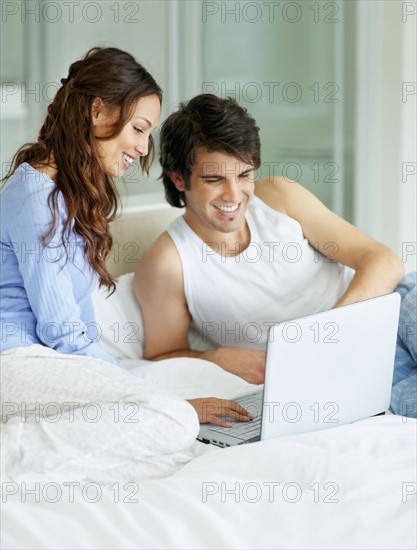 South Africa, Young couple using laptop while sitting on bed. Photo : momentimages