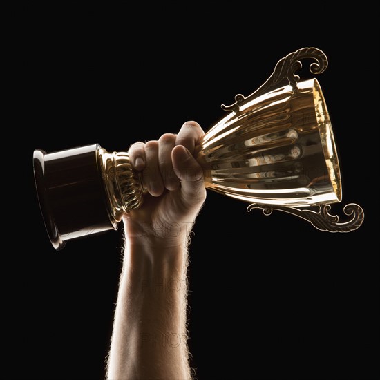 Hand holding trophy on black background. Photo : Mike Kemp