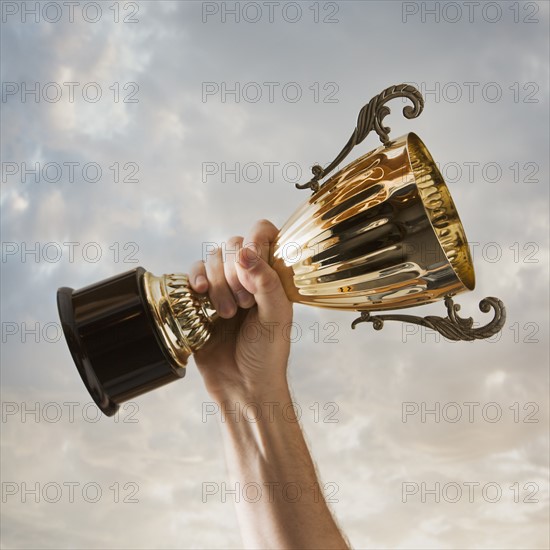 Hand holding trophy against sky. Photo : Mike Kemp