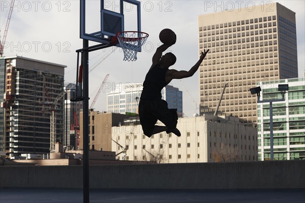 USA, Utah, Salt Lake City, Silhouette of young man playing basketball. Photo : Mike Kemp