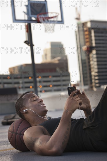 USA, Utah, Salt Lake City, Young man lying on basketball and listening to mp3 player. Photo : Mike Kemp