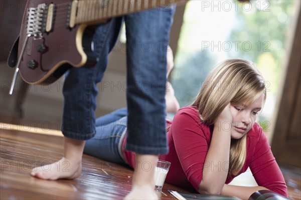 USA, Utah, Girl (10-11) reading magazine while another girl (6-7) playing guitar. Photo : Tim Pannell