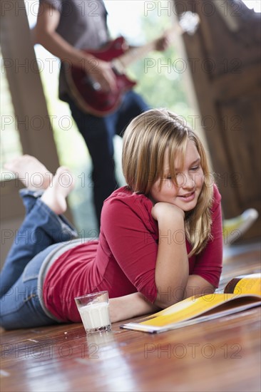 USA, Utah, Girl (10-11) reading magazine while man in the background playing guitar. Photo : Tim Pannell